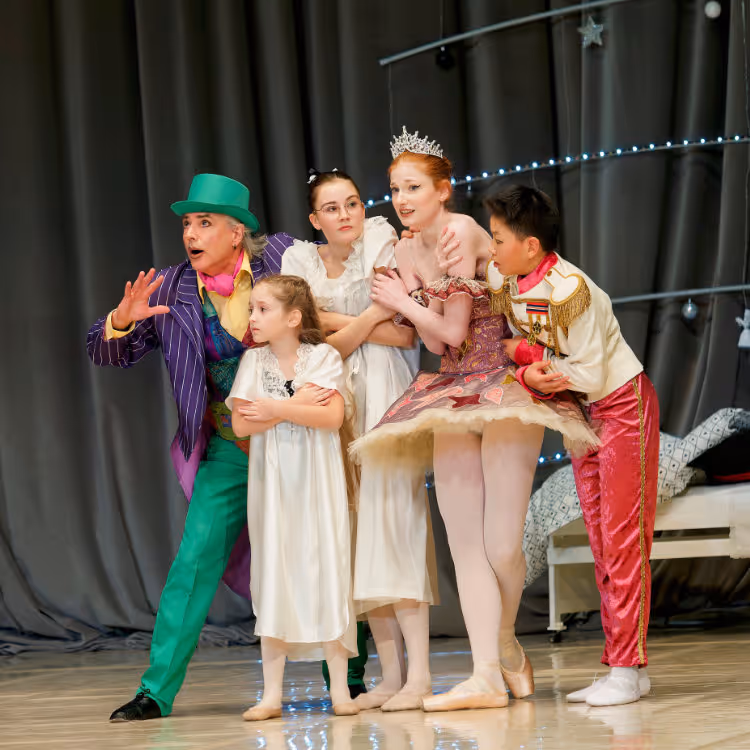Fünf Schauspieler in bunten Kostümen auf Bühne, darunter ein Mann mit grünem Hut, drei Frauen in weißen Kleidern und ein Junge in festlicher Uniform.