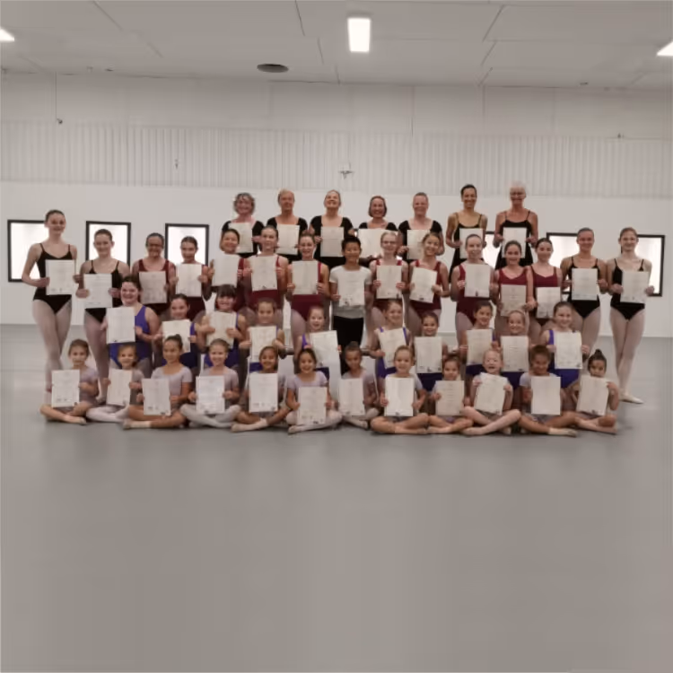 Große Gruppe von Balletttänzerinnen verschiedenen Alters in einem Tanzstudio, die Urkunden halten und lächeln.